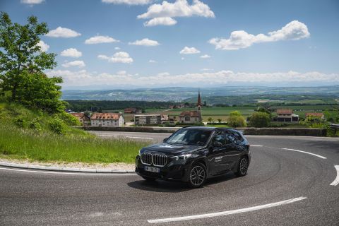 BMW iX1 driving on Swiss country roads with a small village in the background