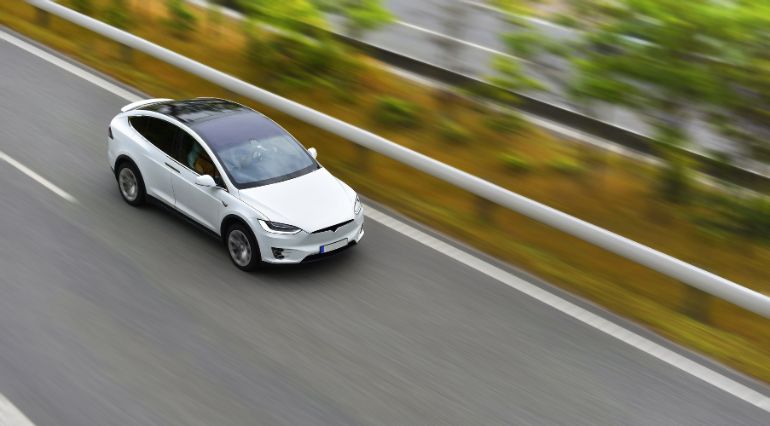 A white EV driving along a dual carriageway