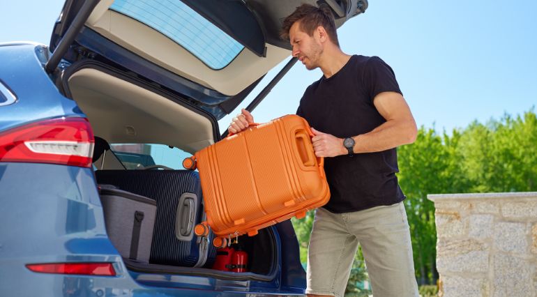 A man loading an orange suitcase into a car boot on sunny day