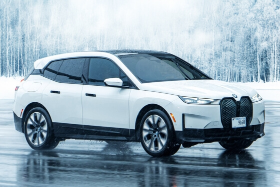 BMW iX on a wet icy road with a snow covered forest behind
