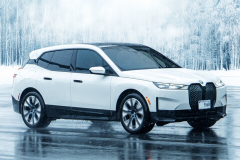 BMW iX on a wet icy road with a snow covered forest behind