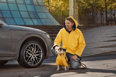 A man and dog both in yellow rain jackets by a grey car