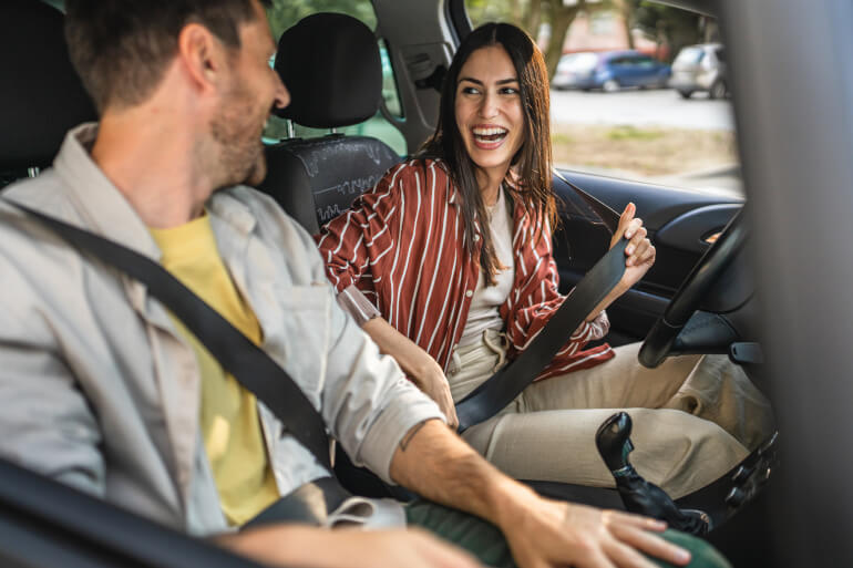A couple getting in a car putting on seatbelts