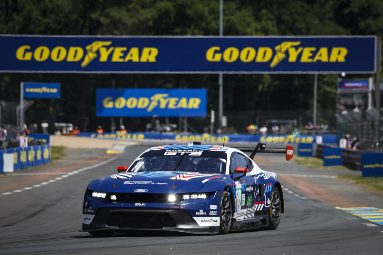 Racing car on a racetrack with a Goodyear banner overhead.
