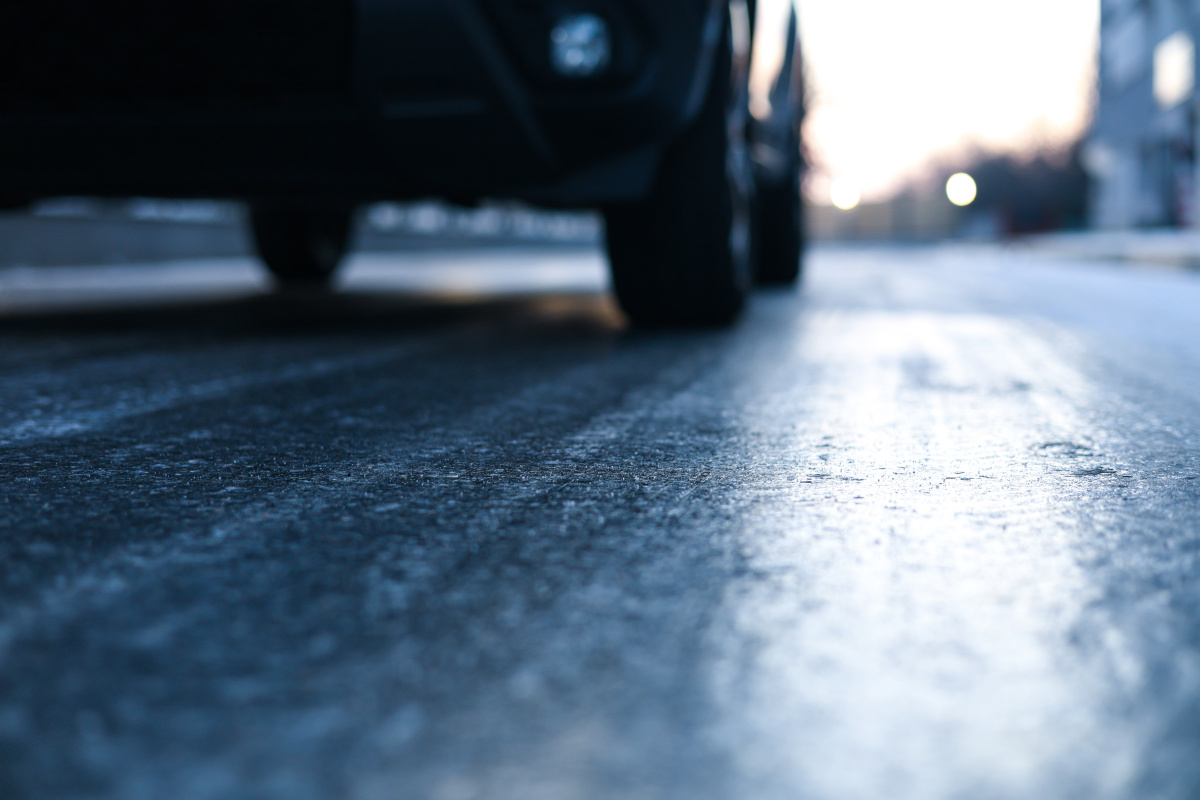 Close-up of an icy road surface with a car in the background