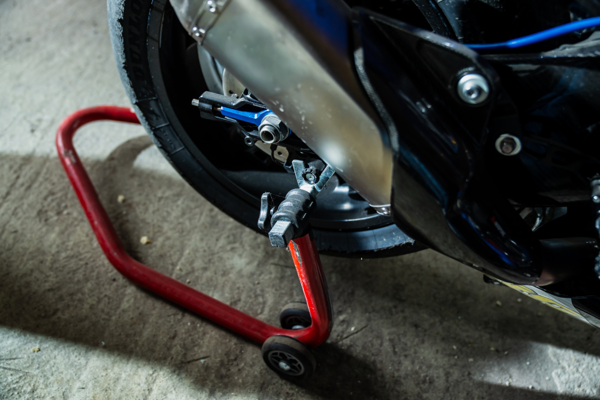 Red paddock stand lifting a motorcycle's rear wheel off a garage floor