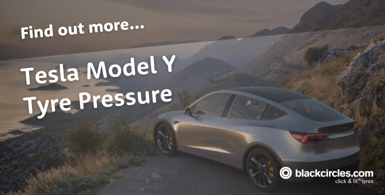 Silver Tesla Model Y parked on a mountain road overlooking the coast at sunset