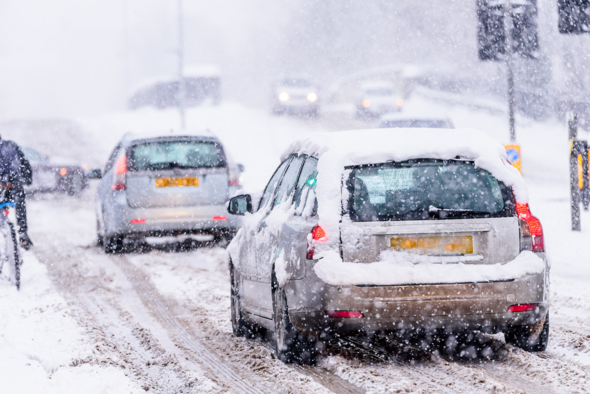 Cars driving slowly on a snowy UK road in heavy snowfall
