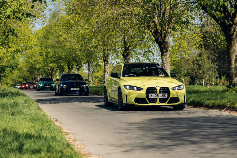 Line of BMW M3s driving down a country road